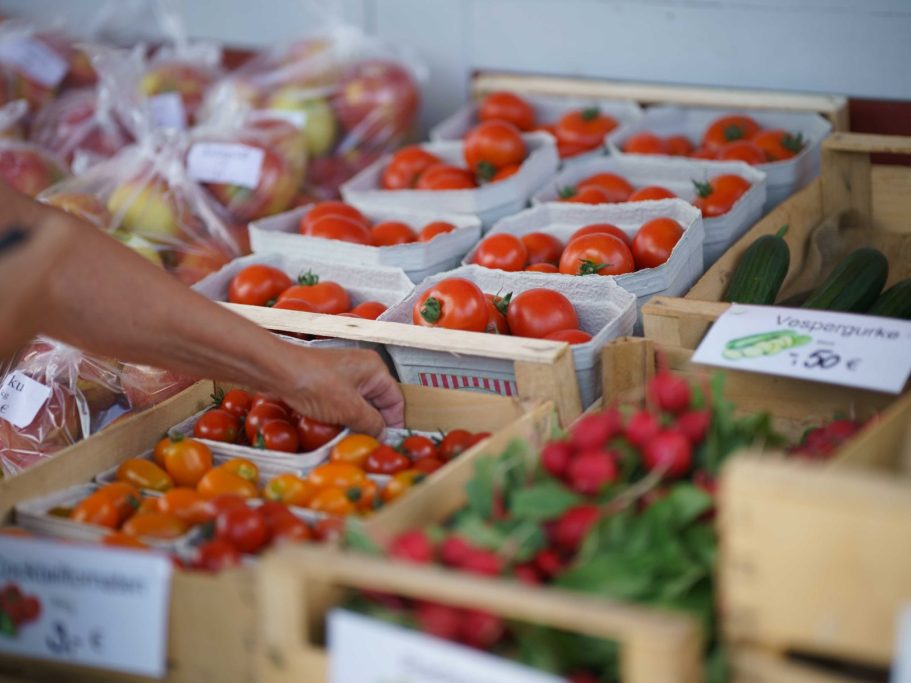 Hofladen Durbach Bunte Gemüse- und Obstkörbe auf einem Marktstand mit einer Hand, die nach Tomaten greift.